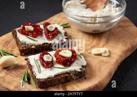 Homemade multigrain bread sandwiches with cream cheese and sun-dried tomatoes on a wooden platter. Healthy eating concept Stock Photo