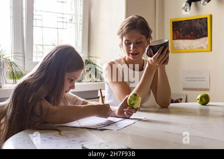 Teenager girl drawing picture on paper sheet or making notes use pen mother talking drinking tea Stock Photo