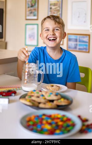 Funny boy eat cookies with round multi-colored sweets and drink milk. Stock Photo