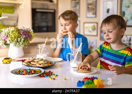 Funny male brothers eat cookies with round multi-colored sweets and drink milk. Stock Photo