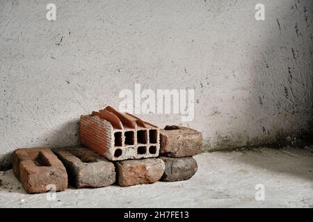 Bundle of red bricks on white concrete and plaster wall and ground. Various red and already used bricks on ground. Stock Photo