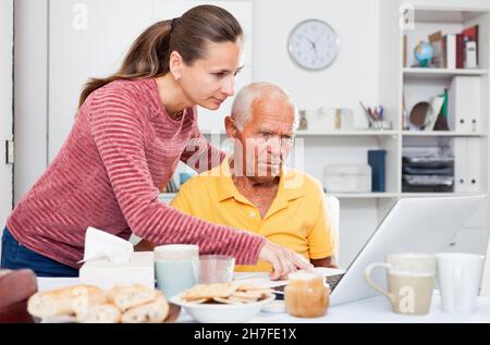 Mature man working at laptop, daughter trying to help him Stock Photo