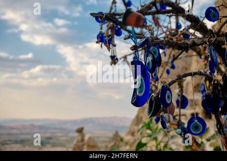 large groups of blue bead worn against the evil eye hanging on trees in edge castle (uchisar) in Cappadocia, gore in Turkey with dramatic cloudscape Stock Photo