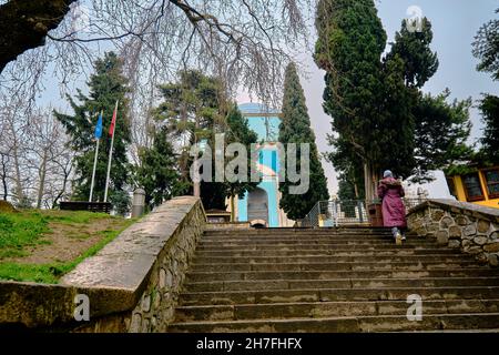 Green tomb (Yesil Turbe) with iznik pottery (cini) or tiles covered tomb wall and walking women with islamic clothes during rain. Stock Photo
