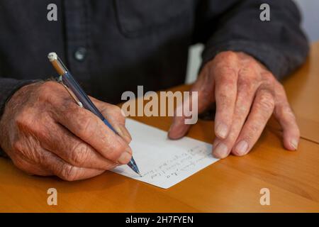 A close up of the hands of an elderly man's hands writing a note MR - Model Released Stock Photo