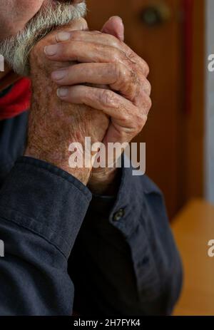 A close up of the hands of an elderly man's hands clasped against his chin MR - Model Released Stock Photo