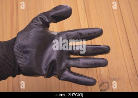 A black construction glove dressed in a man's hand - wooden background Stock Photo