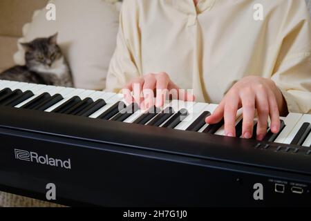 Woman musician playing electronic piano Roland at home on sofa in living room - Moscow, Russia, October 28, 2021 Stock Photo