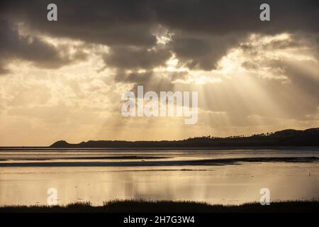 Shafts of sun ray light breaking through clouds at Malltraeth Anglesey, Wales Stock Photo