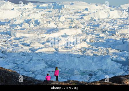 DENMARK. GREENLAND. WEST COAST. TOURISTS IN FRONT OF THE FJORD FULL OF ICEBERGS COMING FROM THE GLACIAR OF ILULISSAT. Stock Photo
