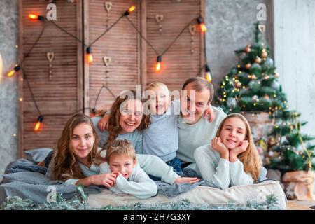 Big Happy family with many kids having fun on the bed near the Christmas tree. Christmas family morning, christmas mood concept Stock Photo