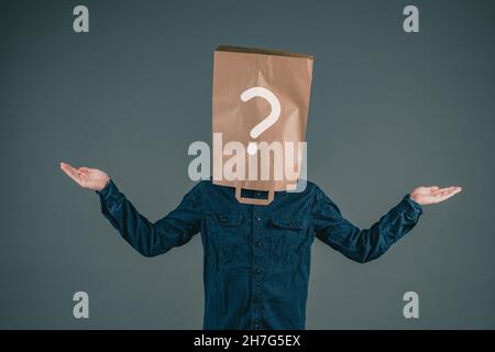 A young man has a paper bag on his head with a question mark, asking why, looking for answers, dark background Stock Photo