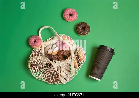 Donuts pink, brown, white in eco string bag and paper cut with coffee on green  Stock Photo