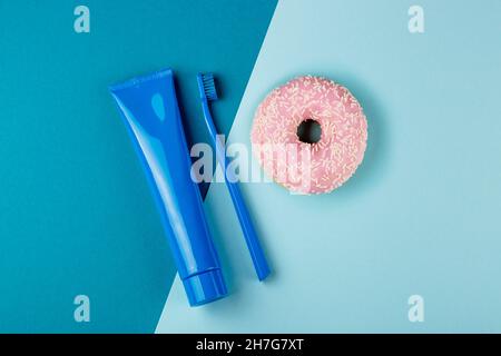Blue tube of toothpaste blue toothbrush and pink donut lie on combined blue background. Top view Stock Photo