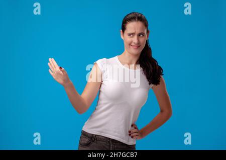 Studio portrait of a young beautiful woman in a white t-shirt against a blue wall background. People sincere emotions. Stock Photo