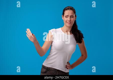 Studio portrait of a young beautiful woman in a white t-shirt against a blue wall background. People sincere emotions. Stock Photo