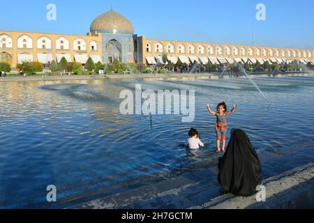 IRAN. ISPAHAN ESFAHAN. EMAM SQUARE. WOMAN IN VEIL LOOKING HER KIDS PLAYING WITH THE WTAER IN THE FOUNTAIN FACING THE CHEICK LOFTOLLAH MOSQUE. Stock Photo