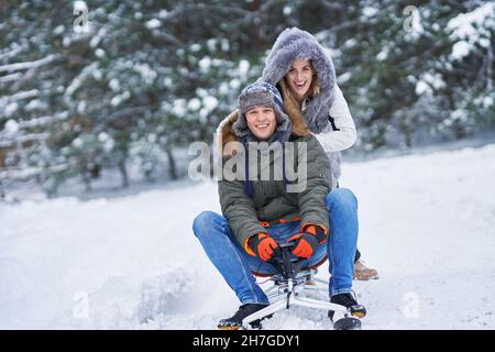 Couple having fun with sledge on snow in winter Stock Photo