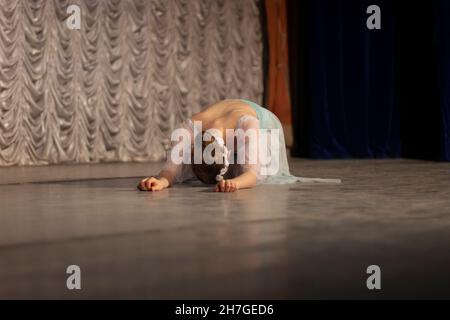 The girl lies on the stage. The ballerina performs. Beautiful movements of the dancer. Stage skills in the girl. Stock Photo