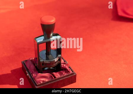 Seal for solemn signing by document. A red tablecloth on the table and an item for stamping envelopes. The predominance of red. Printing press to crea Stock Photo