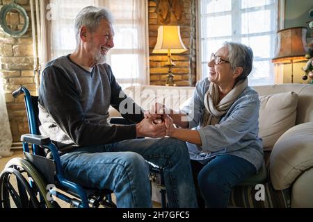 Mature man with disability in wheelchair spending time together with his wife at home Stock Photo