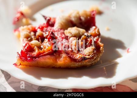 Cake with plums and crumble on plate, sunny day Stock Photo