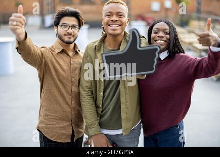 Guy hold phone and show thumb up with friends Stock Photo