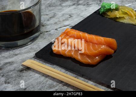 Three Sashimi salmon slices stacked next to ginger and wasabi, on a black tray ready for serving Stock Photo