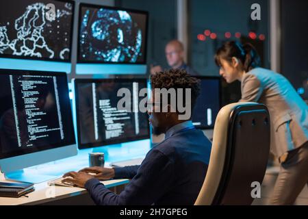 Young it-engineer decoding data while sitting in front of computer monitors and looking at screen of one of them Stock Photo