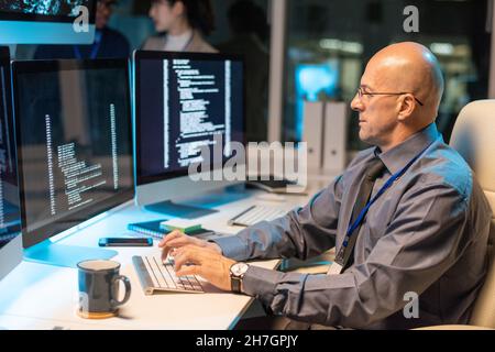 Serious elegant businessman typing and looking at coded data on computer screen while decoding it in office environment Stock Photo