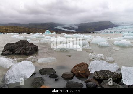 Low angle close up view of some glacial ice and rock in the lagoon in front of the the terminus or end of the Jokulsarlon glacier, Iceland Stock Photo