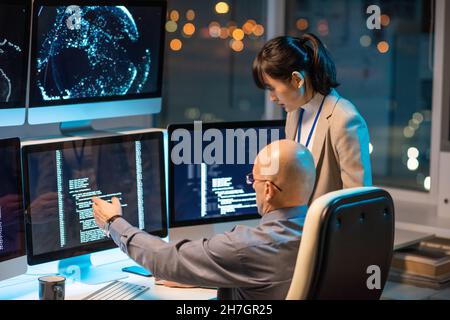 Mature bald businessman showing his young Asian female subordinate new portion of digital data for decoding Stock Photo