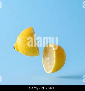 Artistic studio close-up of a fresh juicy lemon cut in half floating with shadow against blue background for copy space Stock Photo