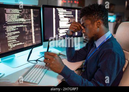 Young tired African businessman sitting by workplace late at night while trying to concentrate and continue working Stock Photo