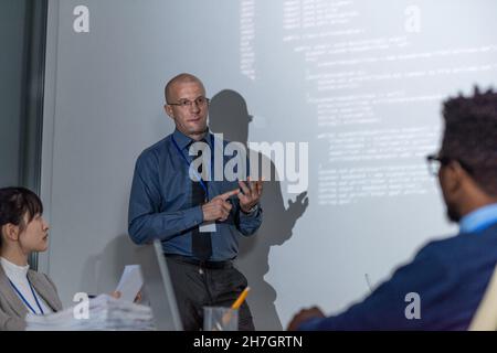 Experienced it-developer in formalwear explaining new way of decoding data to audience during presentation Stock Photo