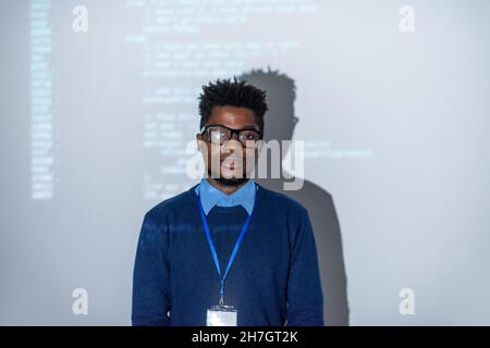 Young confident it-manager or software developer standing against interactive screen with decoded data Stock Photo