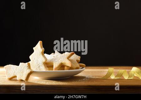 Plate with christmas cookies sprinkled with icing sugar on wooden table with ribbon and black isolated background. Front view. Horizontal composition. Stock Photo