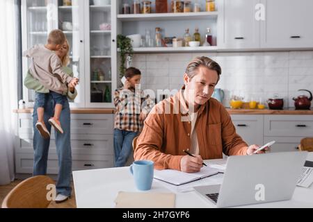 boy talking on mobile phone near mom, brother and dad working in kitchen Stock Photo