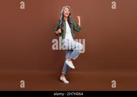 Full size photo of cool old white hairdo lady yell wear khaki shirt jeans shoes isolated on brown color background Stock Photo