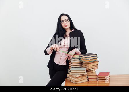 a woman brunette in a business suit teacher with stacks of books Stock Photo