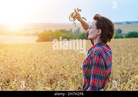 Caucasian female farm worker inspecting soy at field summer evening time somewhere in Ukraine Stock Photo