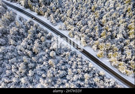 Oberwiesenthal, Germany. 23rd Nov, 2021. Cars drive through the snowy forest on the summit of the Fichtelberg. The meteorologists predict further frosty temperatures for the coming days. (Aerial photo with drone) Credit: Jan Woitas/dpa-Zentralbild/dpa/Alamy Live News Stock Photo