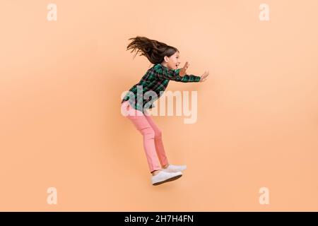 Photo of funky impressed school girl dressed checkered clothes smiling jumping high catching empty space isolated beige color background Stock Photo