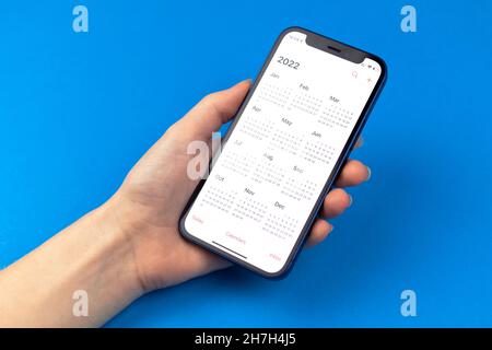 Kharkov, Ukraine - November 17, 2021: Hand holding Apple iPhone with Calendar 2022 app on the screen. Blue background Stock Photo