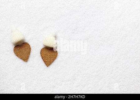 Valentine's Day. Two hearts made of rough fabric in white knitted hats on the snow. Stock Photo