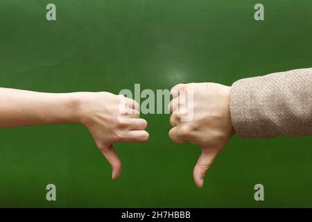 A man's and a woman's hand with thumbs down at the blackboard showing the gesture everything is bad. Stock Photo