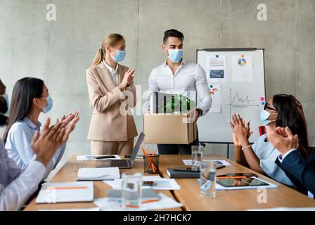Business People In Medical Masks Greeting Arab Male Employee In Their Team Stock Photo
