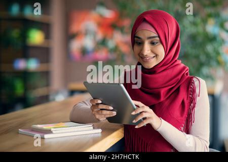 Cheerful muslim lady SMM-manager using digital tablet at cafe Stock Photo
