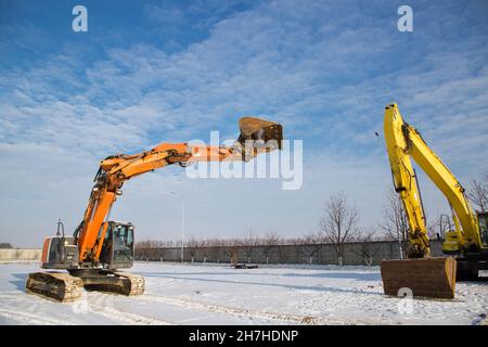 orange and yellow powerful crawler excavators standing at a construction site on snowy ground on a sunny winter day. Rent, lease of working equipment Stock Photo