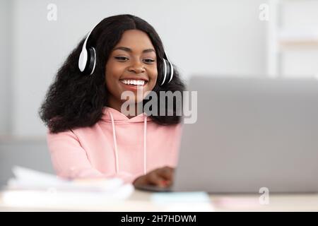Positive black woman attending educational webinar, using laptop and headset Stock Photo
